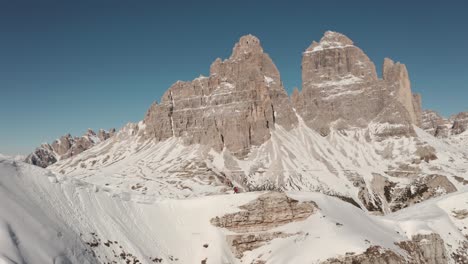 hiker walking along steep snowy ridge line with tre cime dolomites mountains in the background