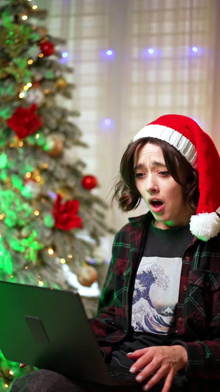 Happy Caucasian lady in Santa cap is focused on the laptop. Woman is excited or surprised looking at the screen. Vertical video.