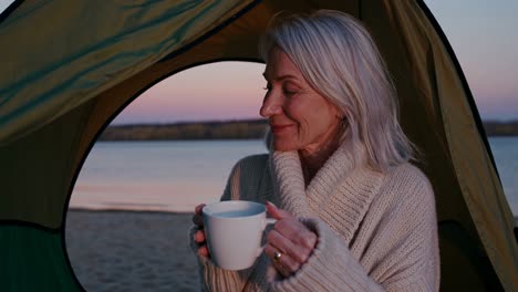 senior woman enjoying a drink in a campsite by the lake at sunset