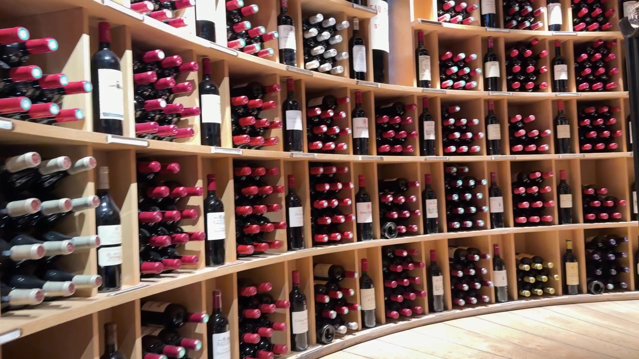 Una lenta carrellata rivela file di bottiglie di vino rosso in una cantina moderna