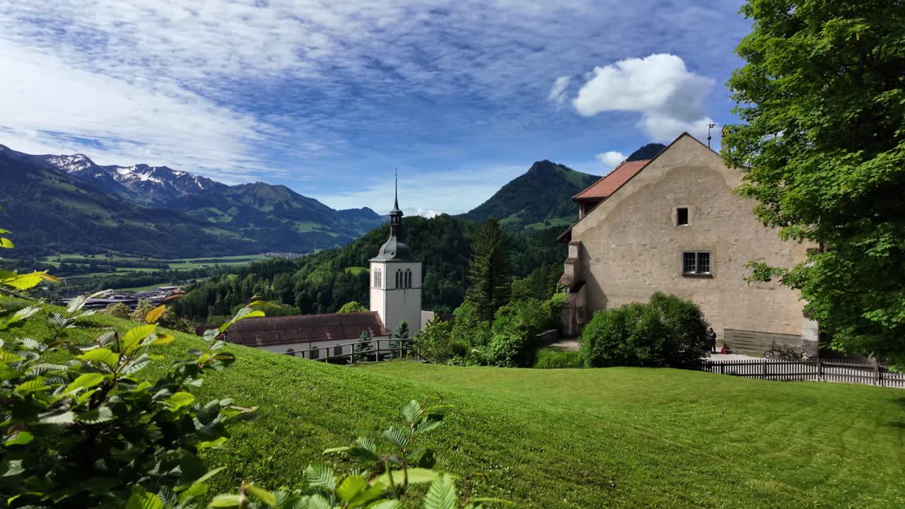 Swiss Alps with a castle in Gruyères. It's summer and the sun is shining. The sky is blue. Clouds cover the sky and nature is blooming