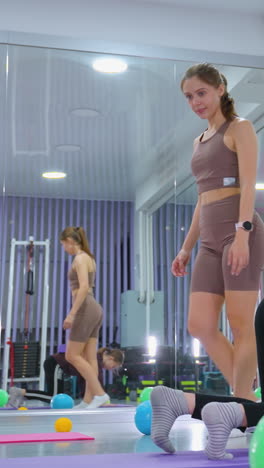 el entrenador de gimnasia ajusta el bloque púrpura en la espalda de la hija mientras se arrastra hacia adelante durante una sesión de entrenamiento, con un gran espejo que refleja sus movimientos en un estudio de fitness bien iluminado