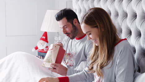 mujer abriendo regalo de collar en la cama en casa como pareja intercambio de regalos en el día de navidad