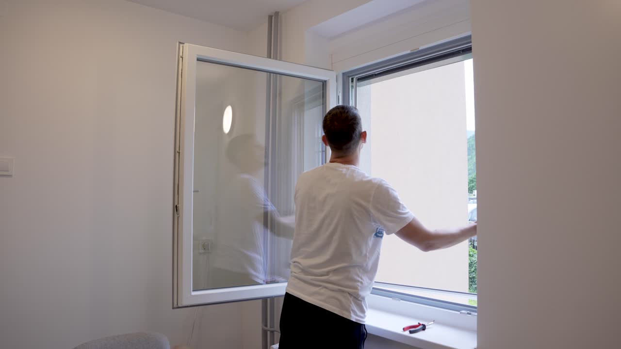 Static timelapse shot of a man installing a fixed mosquito net on a window frame as part of a DIY home improvement project, showing step-by-step progress in fast motion.