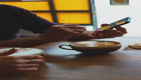 Vertical-Video-Of-Couple-Sitting-At-Table-In-Coffee-Shop-Looking-At-Mobile-Phone-Together