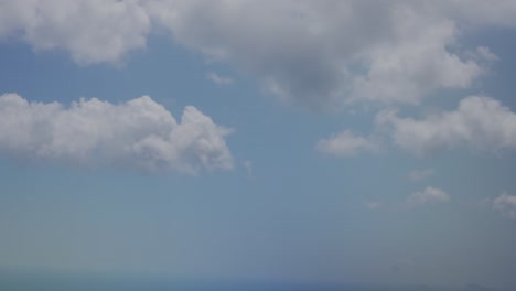 view of large clouds moving above and below outside of chromatic airplane window with water drop on it as plane tilts, santorini, greece, europe