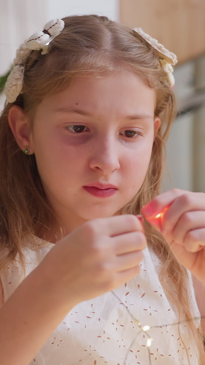 Girl decorates lights, Caucasian woman carefully strings lights in cozy kitchen ambiance, Young woman dressed casually in white is meticulously hanging fairy lights at her kitchen table