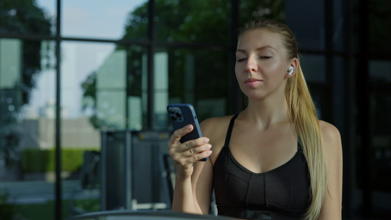 Young woman using smartphone with earbuds at the gym