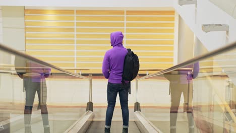 fullshot of man standing on inclined moving walkways, wearing purple hoodie