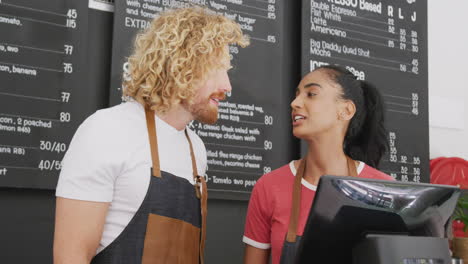 happy diverse male and female baristas talking and using digital till behind counter in cafe