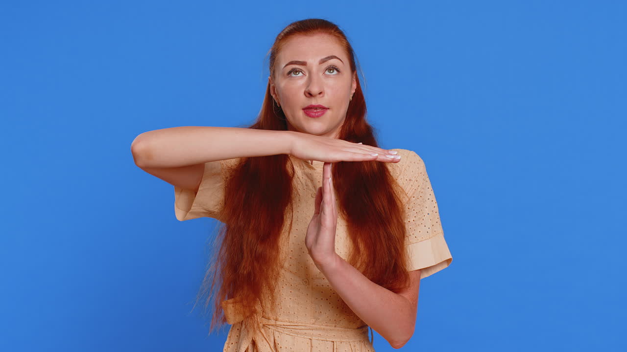 Tired serious upset young redhead woman in dress showing pause gesture limit or stop sign time out