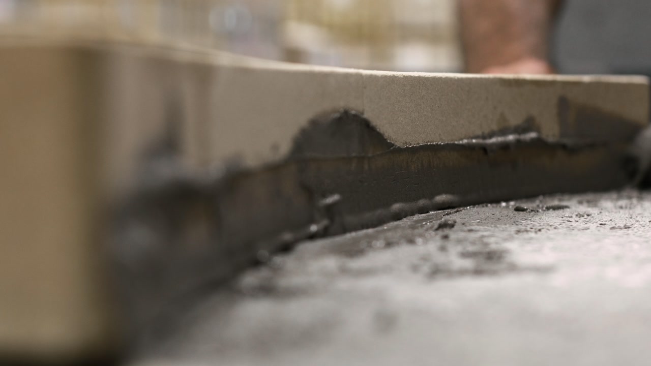 Static extreme close-up shot of fresh grout being applied along the inner seam of a curved pizza oven, emphasizing texture and precision during construction.