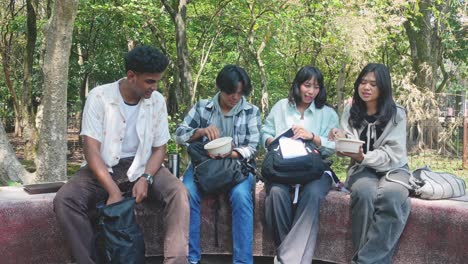 diverse group of university students siting in campus park and having lunch break