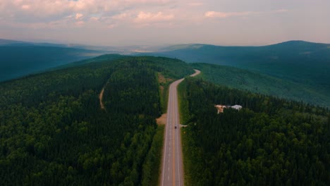 aerial drone flyover 2 lane highway in the middle of nowhere montana with lush green trees and mountains in the background at sunset