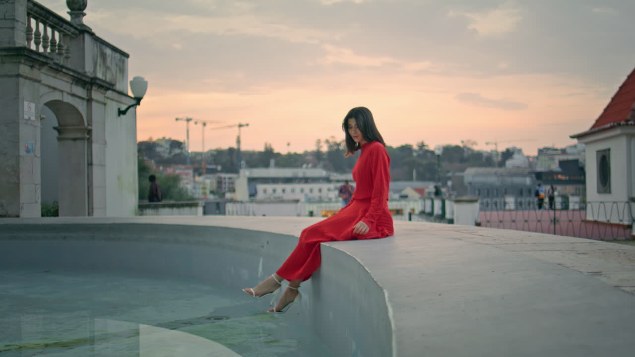 Romantic model sitting fountain posing sunset city. Carefree woman looking water
