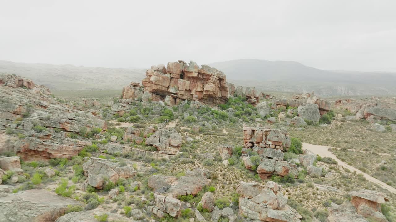 드론이 바위 위에서 뒤로 날아가며 사막 풍경, 세더버그 야생 지역, 남아프리카에서 검은색 오프로드 차량을 볼 수 있습니다.