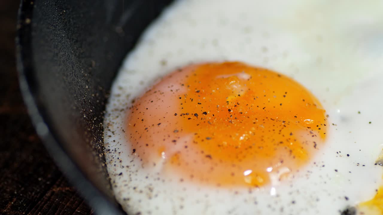 Fried egg in a frying pan sprinkled with ground pepper.
