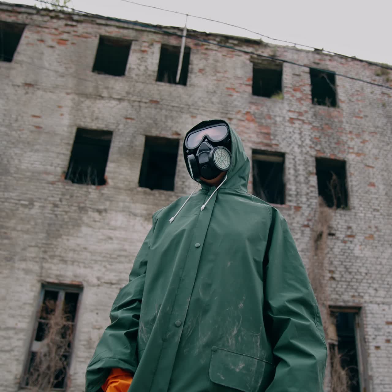 Consequences of chemical attack in the city. Human in safety suit and mask to breathe standing alone on the background of ruined building without windows