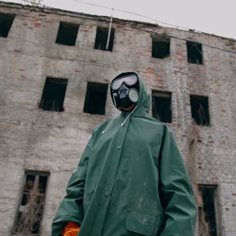 consequences of chemical attack in the city. human in safety suit and mask to breathe standing alone on the background of ruined building without windows