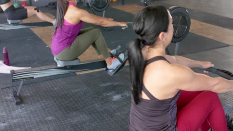 Mujeres-Diversas-Enfocadas-E-Inalteradas-Haciendo-Ejercicio-En-Máquinas-De-Remo-En-El-Gimnasio,-En-Cámara-Lenta