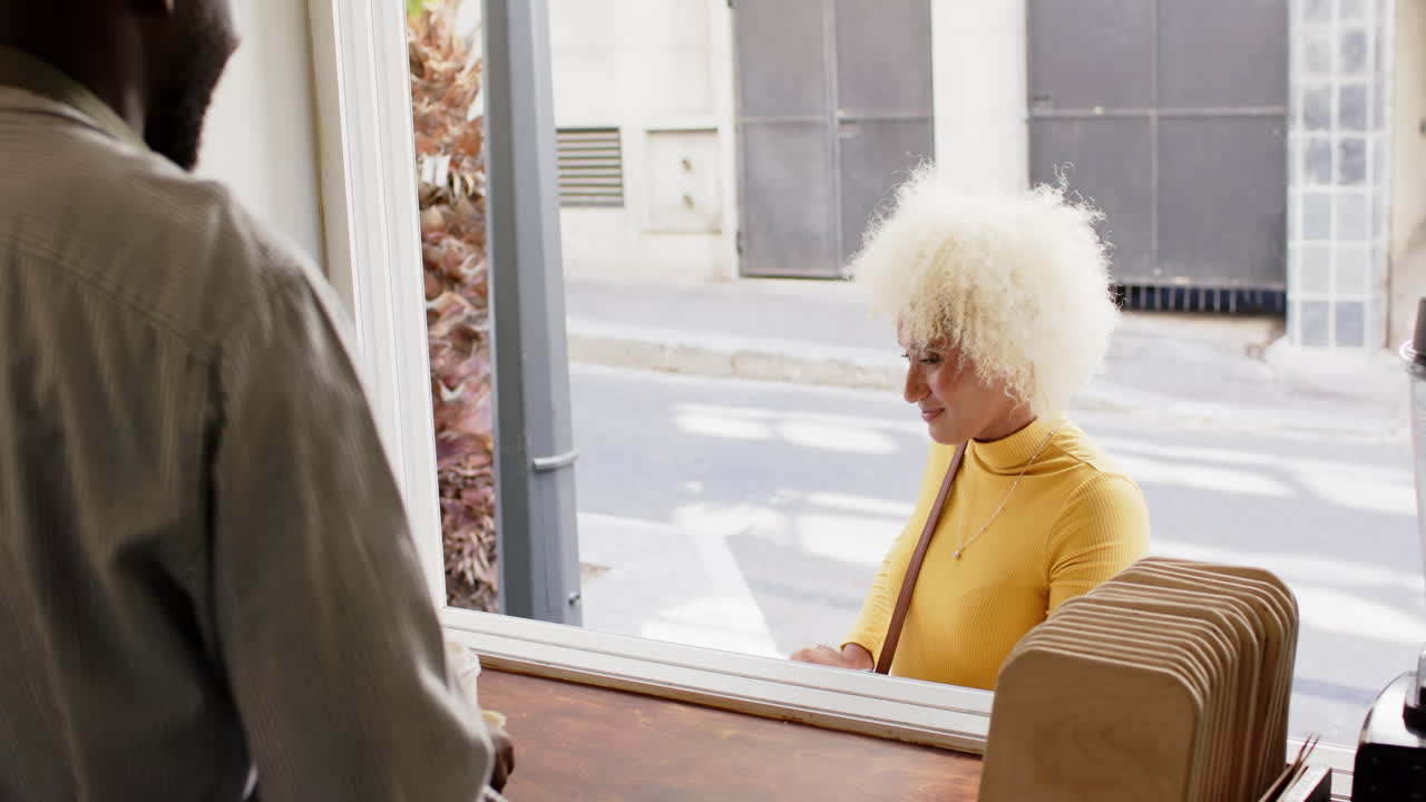 Young African American man serves coffee to go biracial woman in a cafe