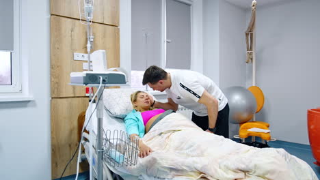 pregnant lady with ctg belt on belly lies in hospital bed. husband bent to sooth her suffering from contractions.