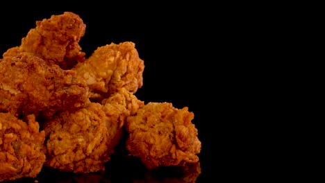 golden, crispy fried chicken pieces are slowly zoomed in on against a black background, highlighting texture, spices, and oily sheen with dramatic studio lighting