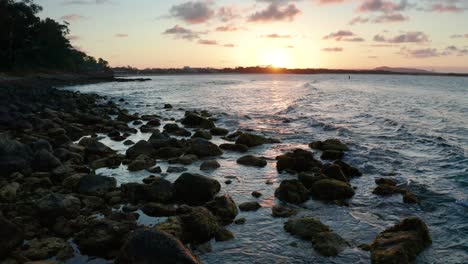 drone floats over rocks on the shore and toward a lone paddleboarder