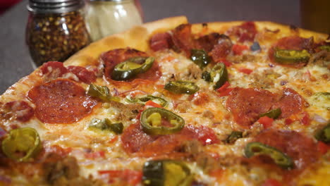 pizza de pepperoni entera de corteza delgada con jalapeños, queso rallado y hojuelas de pimiento rojo triturado en el fondo, cierre deslizante de 4k