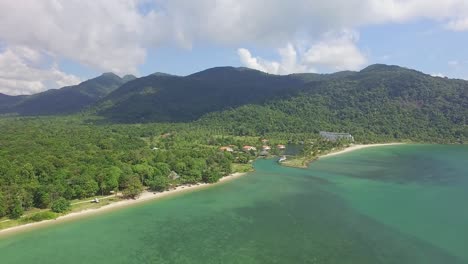 Aerial-back-tracking-shot-of-a-tropical-beach-on-Koh-Chang-showing-mountains-with-lush-dense-Jungle-and-a-sea-view-with-blue-sky