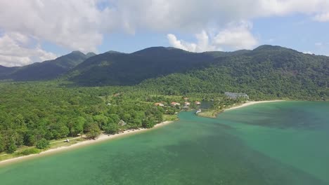 aerial back tracking shot of a tropical beach on koh chang showing mountains with lush dense jungle and a sea view with blue sky