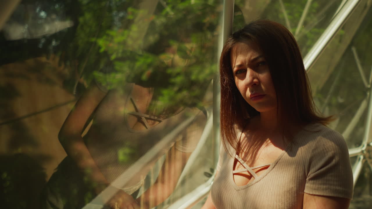 mujer pensativa mira a un lado de pie cerca de la ventana panorámica con vistas al bosque con árboles densos en tiempo soleado. vacaciones y viajes con vistas increíbles. atmósfera pacífica