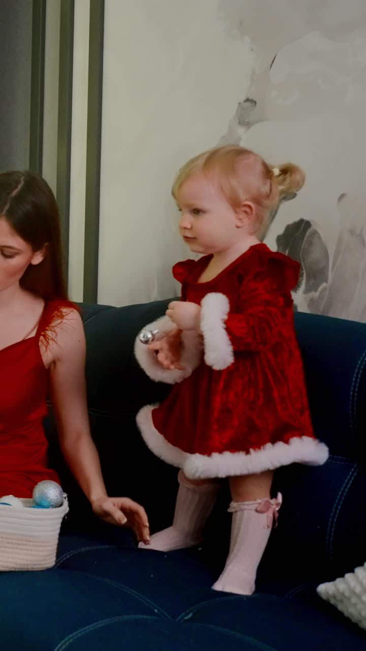 A Joyful Celebration of Childhood: A Little Girl in a Festive Red Dress Brightens the Room with Her Playful Energy and Adorable Smiles, Creating Cherished Memories in a Cozy Setting with Loved Ones