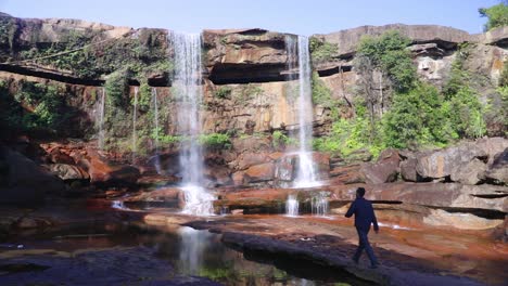 joven disfrutando de la prístina cascada natural que cae desde la cima de la montaña en el día desde un video de ángulo bajo tomado en phe phe fall meghalaya india