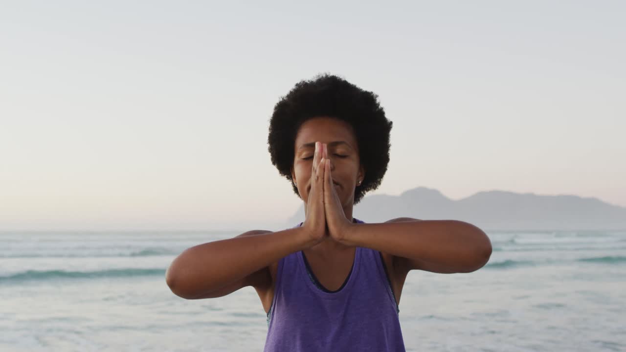 African american woman practicing yoga and meditating on sunny beach