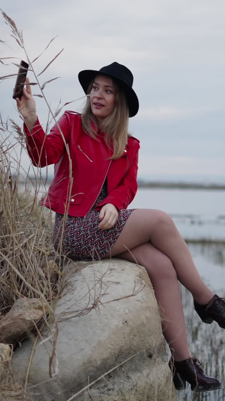 Woman in red jacket taking a selfie by the lake