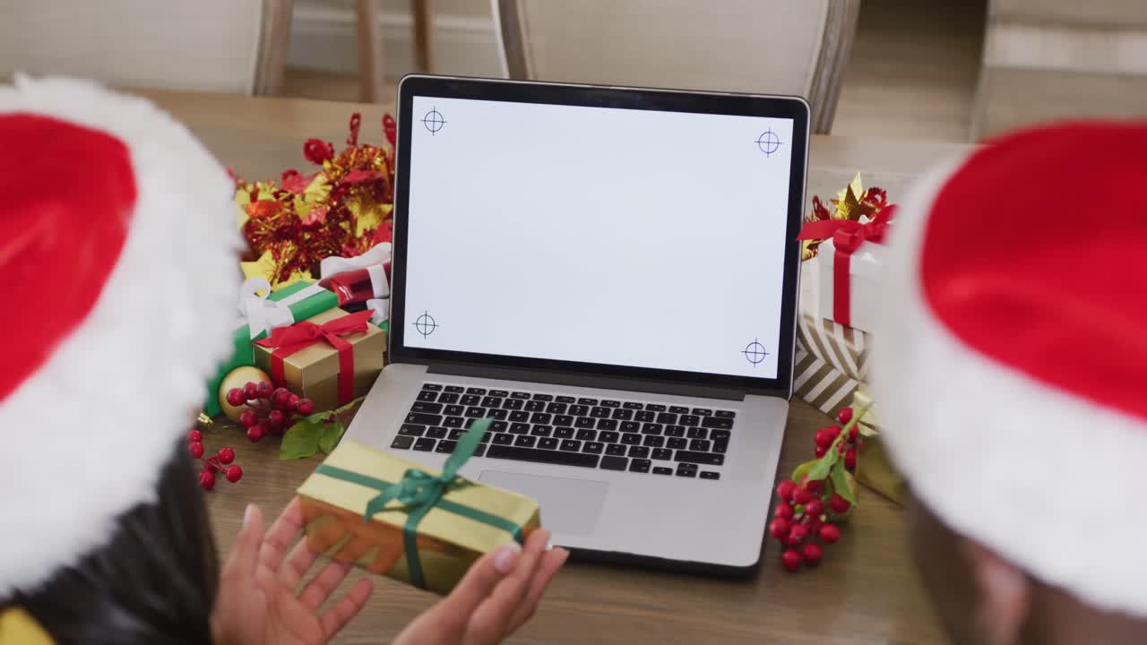 video de una feliz pareja diversa en sombreros de santa haciendo una llamada de video de navidad en una computadora portátil con espacio para copiar.