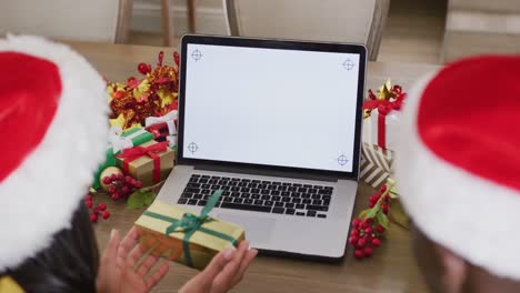 Video-of-happy-diverse-couple-in-santa-hats-making-christmas-video-call-on-laptop-with-copy-space