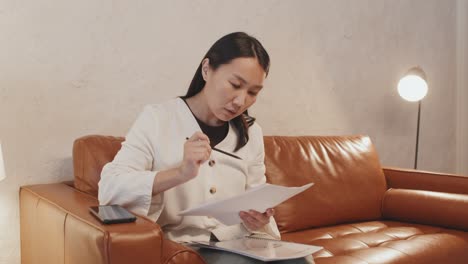 asian woman doing paperwork on couch