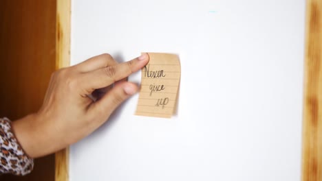 hand placing sticky note on whiteboard with message 'never give up'