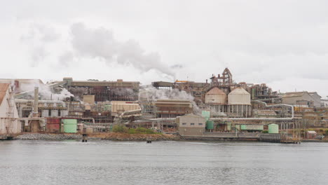 riverside steampunk industrial factory area emitting smoke from smokestack, 4k slow motion