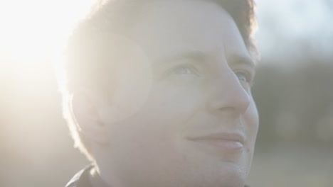 Close-up-shot-of-young-smiling-man-looking-at-the-horizon-with-the-sun-behind-him-flaring-into-the-camera-on-a-cold-spring-morning