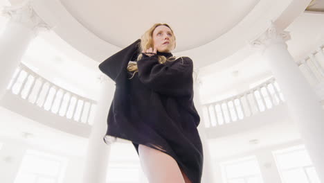 below view of a focused blonde woman in black long sleeve loose pullover and boots performing a contemporary dance in the studio