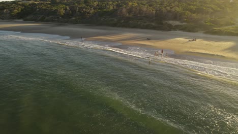 vuelo circular de drones sobre playa grande en uruguay donde los niños juegan en las olas al atardecer