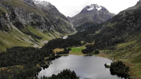 Sobrevuelo-Aéreo-Sobre-Lagh-Da-Cavloc-En-Maloja,-Suiza-Con-Vista-Panorámica-Desde-Los-Picos-De-Engadin-Como-Monte-Forno-Hasta-La-Orilla-Del-Lago