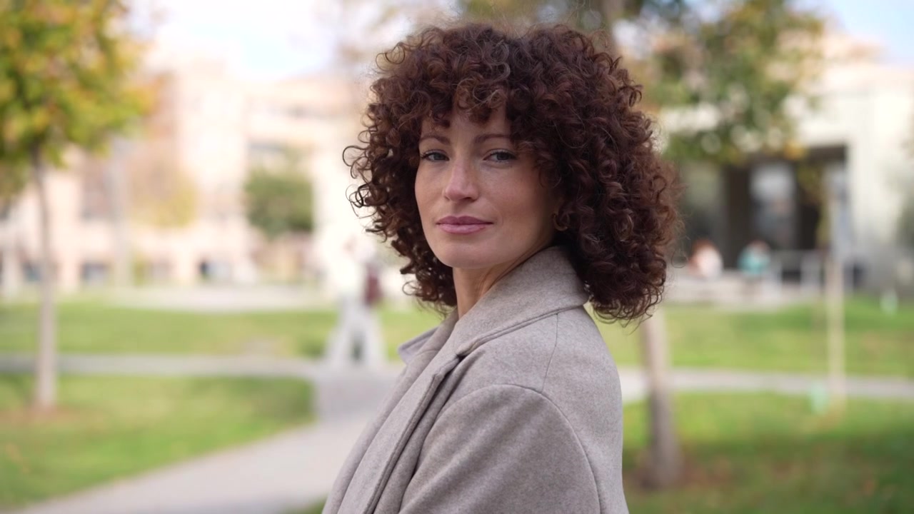 Uma mulher confiante irradiando positividade em um cenário de parque de outono, com cabelo cacheado e energia alegre.