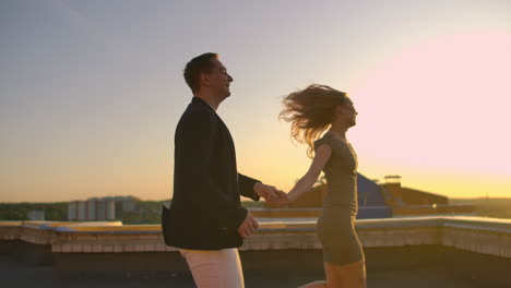 cute lovers laughing running on the roof of the building at sunset on the background of the city and hugging standing at the edge. romance and love