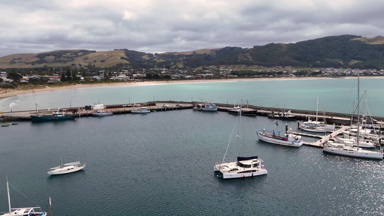 Drone footage captures boats docked at Apollo Bay Harbour with scenic views of the Great Ocean Road coastline