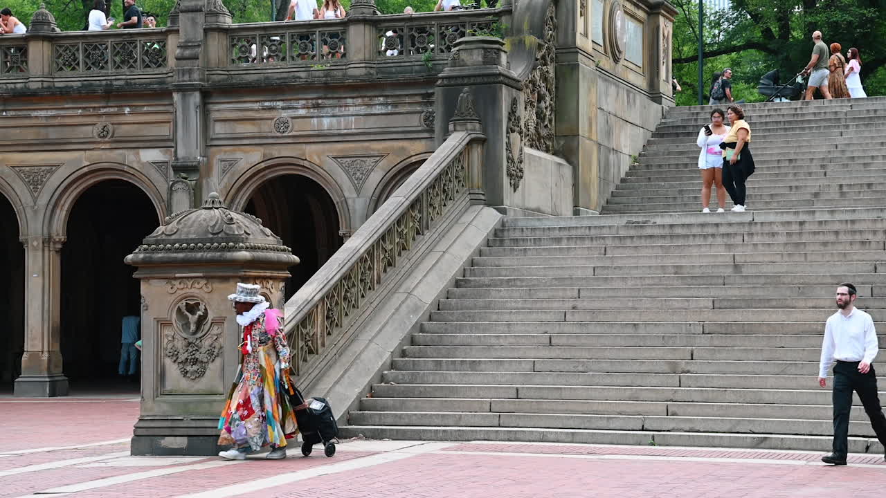 New York, USA, 28 July 2025: Vibrant performer in Central Park. A performer dressed in vibrant clothing walks down the steps at Bethesda Terrace while visitors enjoy the park