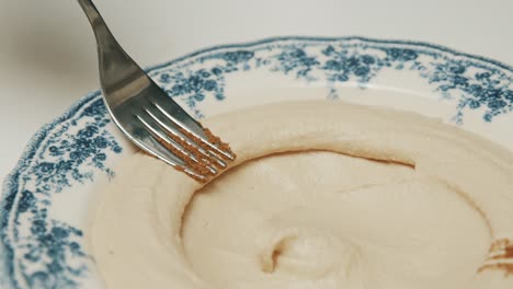inmersión de hummus en un plato, decorándolo con un tenedor - plato árabe tradicional